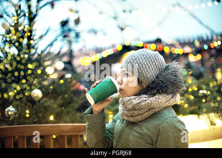 Schöne junge Mädchen mit einem Becher heißen Getränk auf dem Weihnachtsmarkt in Moskau. Stockfoto