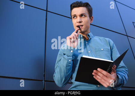 Low Angle View von nachdenklichen jungen Mann mit Notepad und Wegsehen Stockfoto