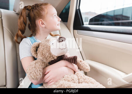 Portrait von fröhlichen Kind umarmen Teddybären und Blick aus Fenster im Auto sitzen Stockfoto