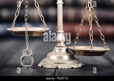 Recht und Gerechtigkeit, Rechtmäßigkeit Konzept, Waage der Gerechtigkeit und Handschellen auf schwarzem Holz- Hintergrund. Stockfoto