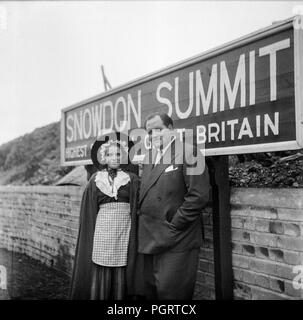 Ein Mann und ein Mädchen in traditionellen walisischen Kostüm gekleidet, am Bahnhof auf dem Gipfel des Snowdon, der höchste Berg in Wales. Foto aus den frühen 1960er Jahren Stockfoto