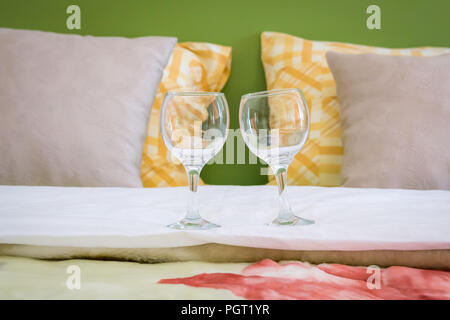 Zwei leere Weingläser stehen auf Doppelbett im Schlafzimmer modernes Hotel. Valentines Tag oder Jubiläum Konzept. Close Up. Stockfoto