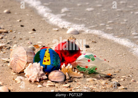 Weihnachtsschmuck und Muscheln an einem Sandstrand mit einer Welle entlang des Golfs von Mexiko für den Urlaub. Stockfoto