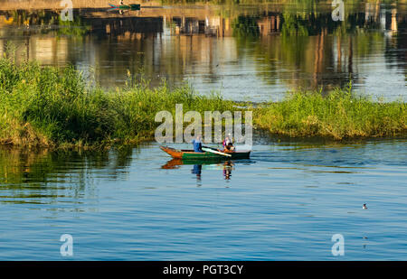 Ägyptische lokaler Mann rudern altes Boot mit Jungen im frühen Sonnenlicht, mit Wasser Reflexionen, Nil, Ägypten, Afrika Stockfoto