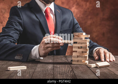 Unternehmer zieht Blocks von hölzernen Turm. Vorstellung von Gleichgewicht und die Planung in Unternehmen. Stockfoto