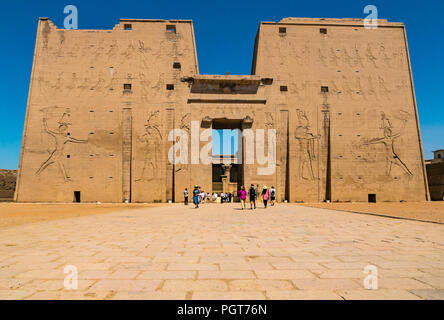 Geschnitzte ägyptische Abbildung Hieroglyphen auf äußeren Eingang pylon, dem Tor des Tempels von Edfu mit Touristen, Edfu, Ägypten, Afrika Stockfoto