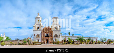 Vordere Querformat der Mission Xavier, unter Licht blauer Himmel mit weißen flauschigen Wolken. Eine abgeschlossene Glockenturm und eine nicht beendete, grünen Bäumen. Stockfoto