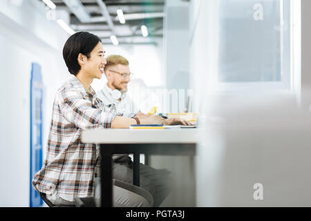 Freundliche Männer lächelnd während der Arbeit an Laptops in Coworking Space Stockfoto