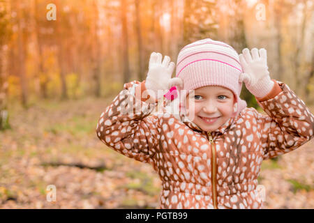 Ein lustiges Mädchen, die in einem warmen Mantel bekleidet steht mit einem bösen Gesicht, ein Baby ist ein Tiger oder ein Reh. Lustige niedliche Kind Gesichter im Herbst Wald, Outdoor. Herbst Jahreszeit Stockfoto