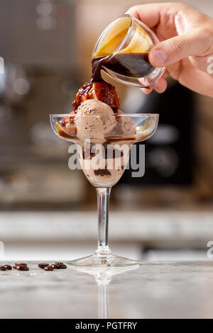 Des Menschen Hand gießen Espresso Kaffee in das Glas mit Schokolade Eis Schaufeln, Affogato Rezept Stockfoto