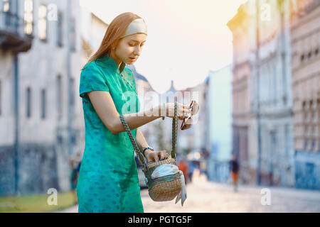 Junge schöne modische Frau in grün Kleid auf der Suche nach etwas in Ihrer Handtasche auf einer Straße der alten Stadt. Weibliche Mode. Stadt lifestyl Stockfoto