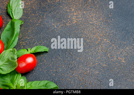 Viele verstreute Grüne frische Basilikumblätter und Kirschtomaten auf einem dunklen rostigen Hintergrund, Nahaufnahme, Ansicht von Oben, kopieren Raum Stockfoto