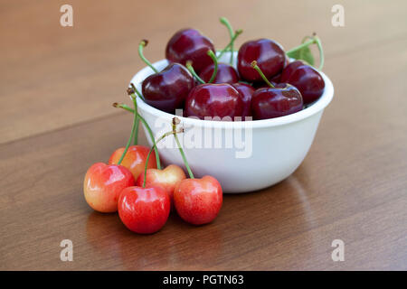 Rote reife Kirschen in eine Schüssel und rainier Kirschen auf Tisch Stockfoto