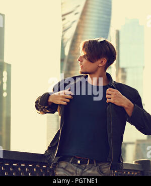 Denken gutaussehenden jungen Mann zu Fuß in fashion jeans und Dressing die schwarze Jacke an Stadtzentrum Hintergrund. Getönte Farbe vintage Portrait Stockfoto