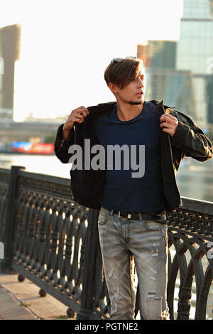 Denken gutaussehenden jungen Mann zu Fuß in fashion jeans und Dressing die schwarze Jacke an Stadtzentrum Hintergrund. Stockfoto