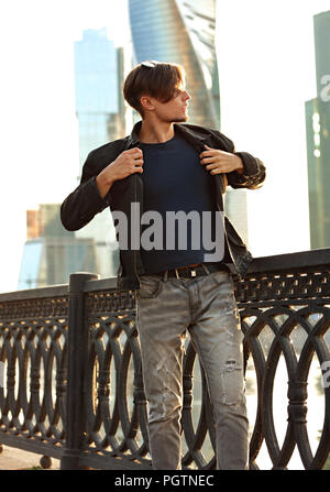 Denken gutaussehenden jungen Mann zu Fuß in fashion jeans und Dressing die schwarze Jacke an Stadtzentrum Hintergrund. Stockfoto