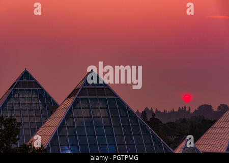 Sun steigt durch Rauch Himmel, Muttart Conservatory Pyramiden, Edmonton, Alberta, Kanada. Stockfoto