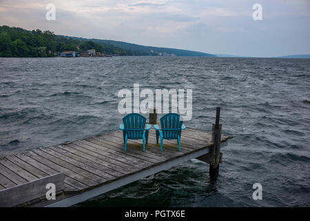 Raue Gewässer, Abbruch in einen Pier mit zwei Kunststoff und blau Adirondack Garten Stühle, als ein Sturm kommt in über Seneca Lake in Watkins Glen, New York. Stockfoto