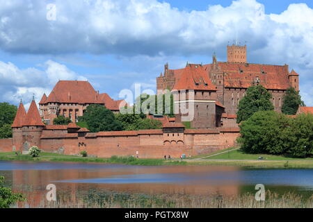 Panoramablick auf die Gotische Teutonische Schloß in Malbork, Polen, vom Fluss Fluß Nogat Bank, schöne wirbelnde Wolken im Himmel. Stockfoto