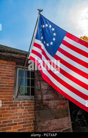 Die dreizehn Sterne Kolonialzeit amerikanische Flagge als Betsy Ross Flagge zu einem alten Backsteingebäude in Peacham, Vermont, United States angefügte bekannt. Stockfoto