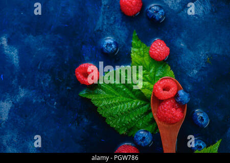 Sommer Beeren in Holzlöffel Ansicht von oben. Himbeeren und Blaubeeren mix auf einem dunkelblauen nass Hintergrund mit kopieren. Zutaten von oben Stockfoto