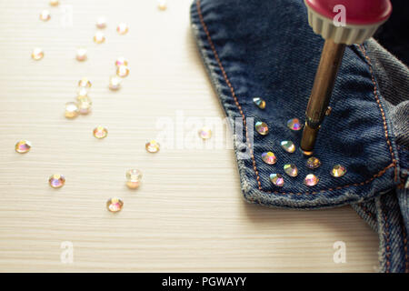 Handgefertigte Dekorationen. Ein Prozess der löten Glitzersteinchen an den Kragen eines denim Jacke von Lötkolben Stockfoto