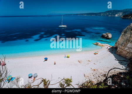 Fteri Strand, Kefalonia Kefalonia, Griechenland. Weißen Katamaran Yacht in klaren tiefblauen Meer Wasser mit erstaunlichen dunkle Muster auf der Unterseite. Touristen am Sandstrand in der Nähe der blauen Lagune Stockfoto