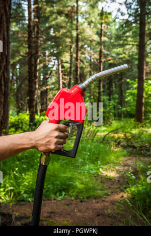Eine menschliche Hand mit einem Benzin pumpe Düse in einen Wald. Konzept, ökologische Fragen rund um Erdöl. Stockfoto
