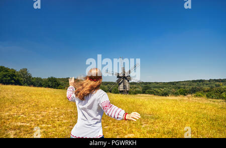 Schöne Ukrainische Mädchen zu laufen, um hölzerne Windmühle in weißen ethnischen Shirt auf nationaler Architektur Museum in Pirogowo. Kiew, Ukraine Stockfoto