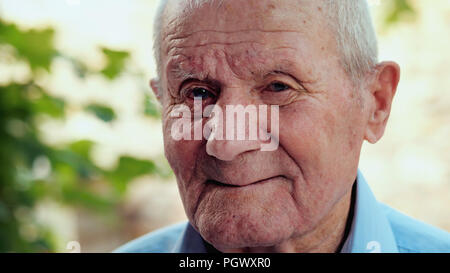 Sehr alter Mann Portrait mit Emotionen. Großvater lächelt und schaut in die Kamera. Porträt: Alter, Senioren, Senior. Nahaufnahme der alte Mann sitzt alleine im Freien. Stockfoto