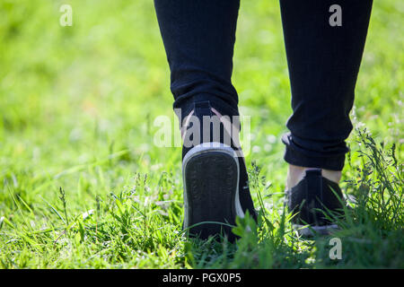 Mann Spaziergänge entlang Gras in Gummi Turnschuhe und eine schwarze Hose, Ansicht von hinten Stockfoto