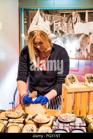 Zaandam, Niederlande, 28-Aug-2018: Mädchen in traditionell niederländische Kleid Schneiden Sie den Käse in einem Käse shop zu schmecken und für den Verkauf in einem Shop in Zaandam Zaandam ist berühmt von Zaanse Schans, alte traditionelle holländische Häuser Stockfoto