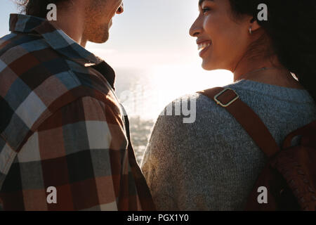 Nahaufnahme des jungen Paares im Freien stehen an jedem anderen suchen und lächelnd. Glücklich der Mann und die Frau im Freien mit Blick auf das Meer im Hintergrund. Stockfoto