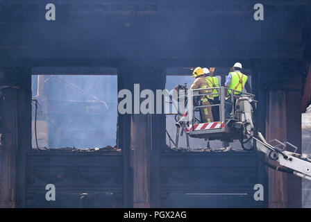 Ein Feuerwehrmann und Ingenieure überprüfen Der verkohlten Fassade des Primark store in der historischen 5-stöckige Bankgebäude in Belfast City Center, nach dem Zusammenbruch der internen Etagen in einem verheerenden Brand, der am Dienstag brach. Stockfoto