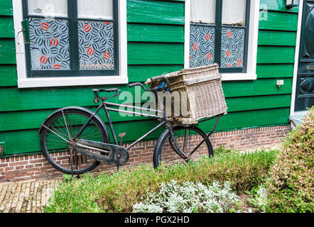 Altes Fahrrad mit einem abgenutzten Weidenkorb in Front vor der alten Holzhaus aus grün lackiertem Holz und roten und schwarzen Vorhängen Stockfoto