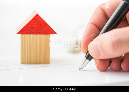 Ein Spielzeug Holz- Gebäude in der Nähe einer Hand schreiben oder einen Kugelschreiber. Stockfoto