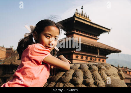 Bhaktapur, Tal von Kathmandu, Nepal Bagmati,: ein Kind Mädchen sitzt auf einer der Statuen der Nyatapola Tempel, lächelt in die Kamera mit dem Bhaira Stockfoto