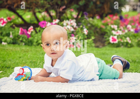 Portrait von cute adorable kleinen indischen Asiatischen oder Orientalischen baby boy im weißen Hemd mit auf dem Boden mit Spielzeug in Park draußen auf hellen s Stockfoto