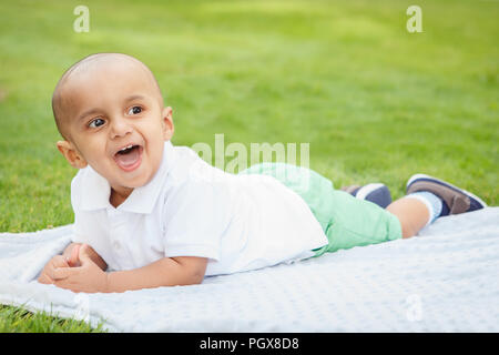 Portrait von cute adorable kleinen indischen Asiatischen oder Orientalischen baby boy im weißen Hemd Festlegung auf Erde in Park draußen auf hellen Sommertag Stockfoto