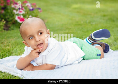 Portrait von cute adorable kleinen indischen Asiatischen oder Orientalischen baby boy im weißen Hemd Festlegung auf Erde in Park draußen auf hellen Sommertag Stockfoto