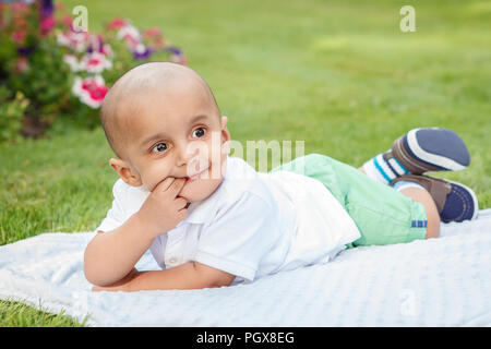 Portrait von cute adorable kleinen indischen Asiatischen oder Orientalischen baby boy im weißen Hemd Festlegung auf Erde in Park draußen auf hellen Sommertag Stockfoto