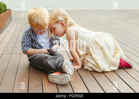 Zwei cute adorable White kaukasischen Kleinkinder Junge und Mädchen sitzen zusammen und Spielen auf dem Handy digital Tablet. Candid Lebensstil früh Stockfoto