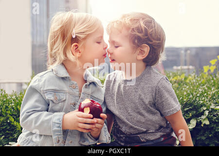 Group Portrait von zwei weissen Kaukasischen cute adorable lustig Kinder Kleinkinder sitzen zusammen teilen Apple essen. Kinder küssen einander. Liebe Freunde Stockfoto