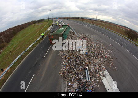 Ein Lkw umkippt und Leckagen ist es Laden der Verwertung von Abfällen über die neue Fahrbahn der Großen Yorkshire in Doncaster, South Yorkshire Stockfoto