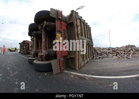 Ein Lkw umkippt und Leckagen ist es Laden der Verwertung von Abfällen über die neue Fahrbahn der Großen Yorkshire in Doncaster, South Yorkshire Stockfoto