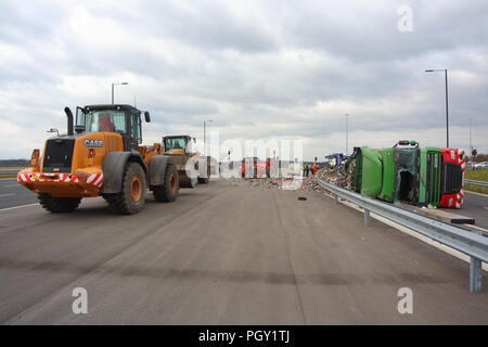 Ein Lkw umkippt und Leckagen ist es Laden der Verwertung von Abfällen über die neue Fahrbahn der Großen Yorkshire in Doncaster, South Yorkshire Stockfoto