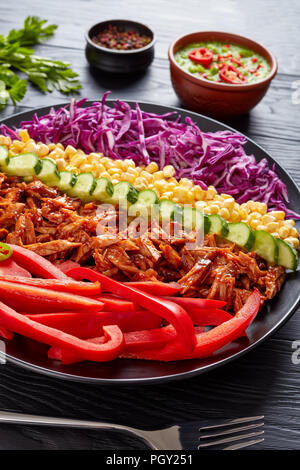 Bbq zog Schweinefleisch Salat mit angeordneten Reihen von krautsalat, Mais, Paprika, Gurke und jalapeno auf schwarzem Teller serviert auf einem Holztisch mit Avocado Stockfoto