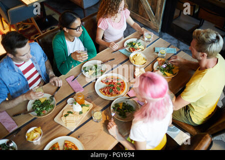 Überblick über Holz- serviert Tisch mit leckeren Mahlzeit und eine Gruppe von Freunden sitzen um das Abendessen und Stockfoto