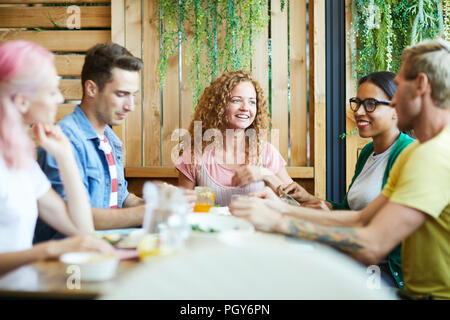 Glückliche Mädchen und Jungs in der casualwear sitzen, Tisch serviert, während Mittag- und in Chat Stockfoto
