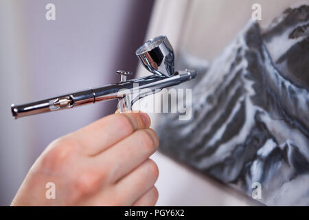 Spritzpistole eine Bürste in weiblicher Hand, Malerei Berge mit aerograph, Nahaufnahme Stockfoto